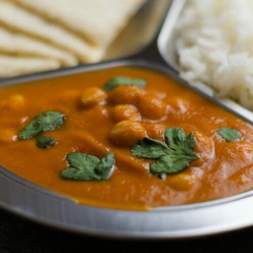 chana masala served in a 3 compartment silver tray with rice and flatbread