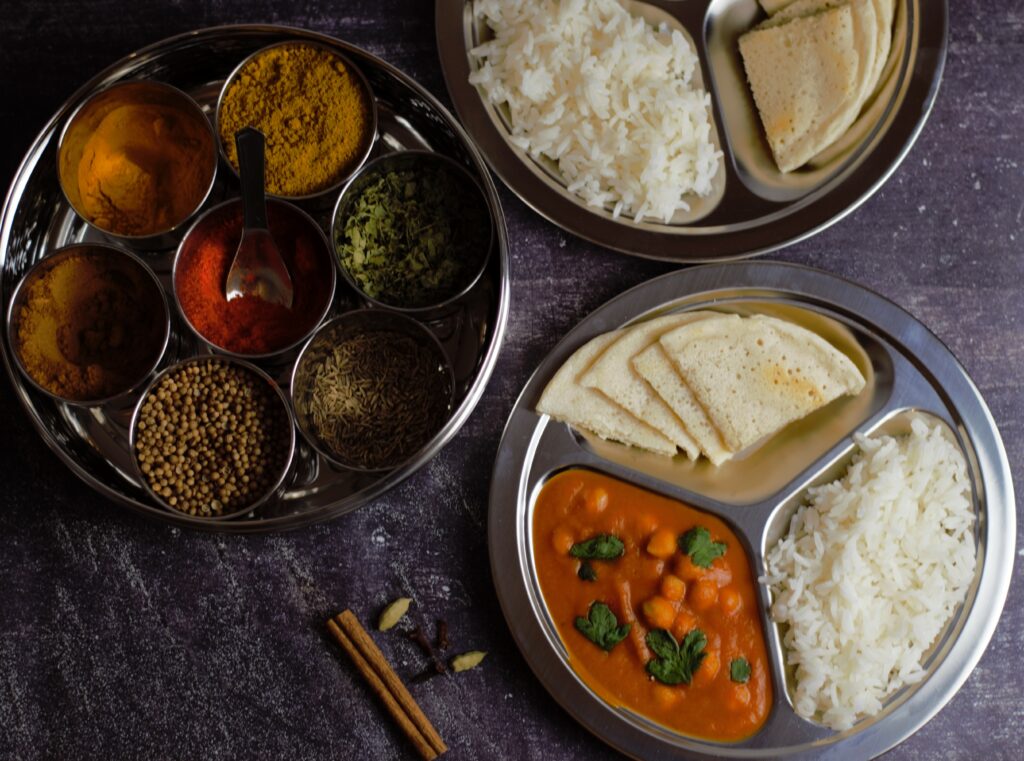 Chana Masala on a silver plate next to jars of Indian spices.